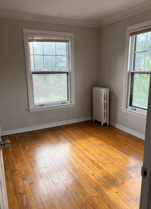 an empty room with wooden floors and two windows