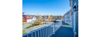 A balcony with a railing overlooks a parking lot and a row of houses.