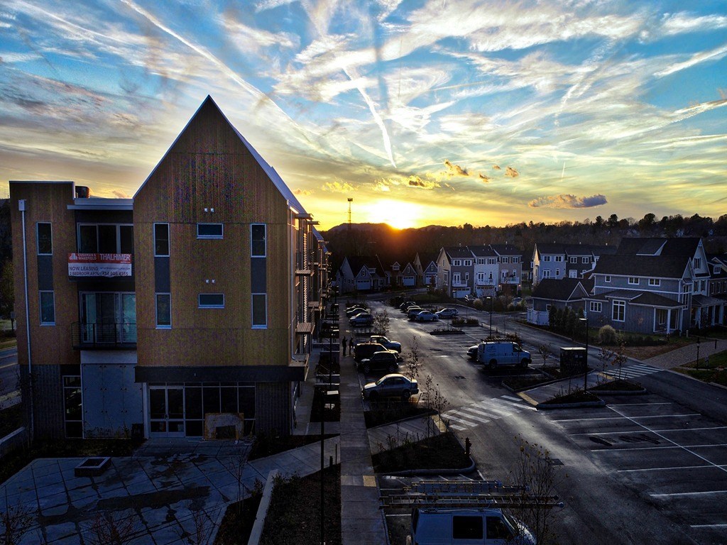 the sun sets over a city with a building and a parking lot