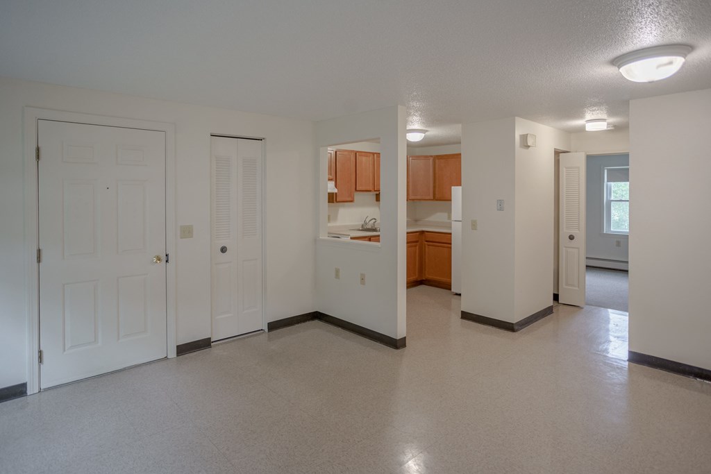 an empty living room with a kitchen in the background