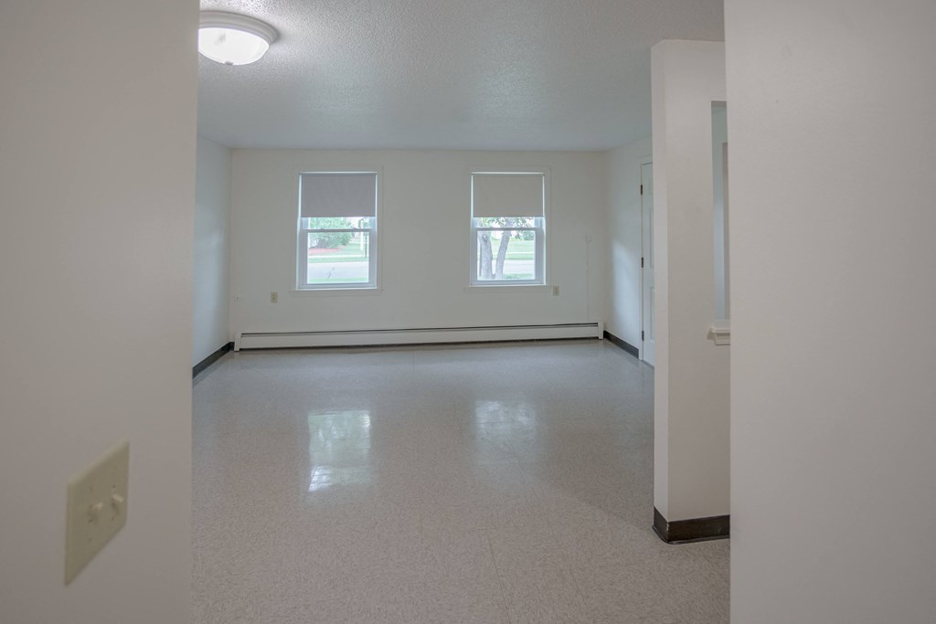 the living room of an empty house with a white floor and two windows