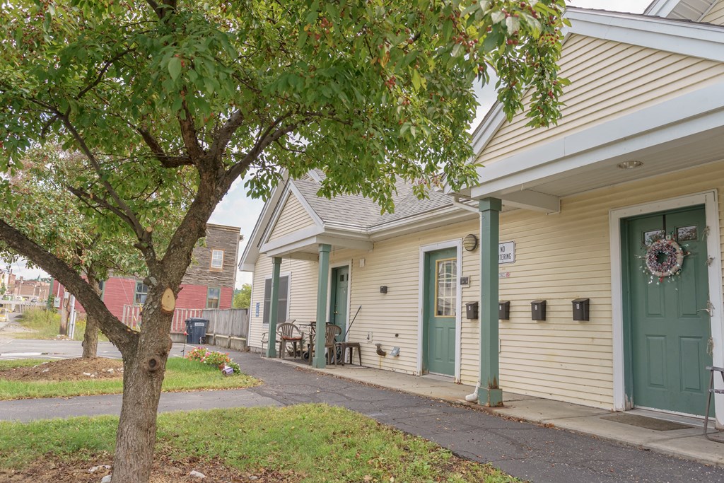 the front of a yellow house with a green door and a tree