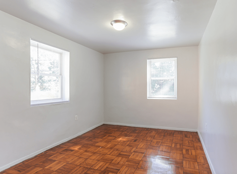 A room with wooden flooring and two windows.