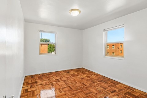 A room with wooden flooring and two windows.