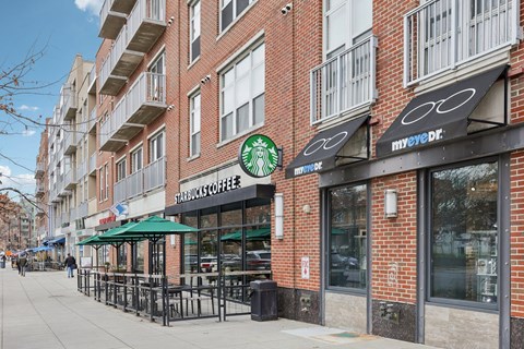 A Starbucks Coffee shop is located on a sidewalk in front of a brick building.