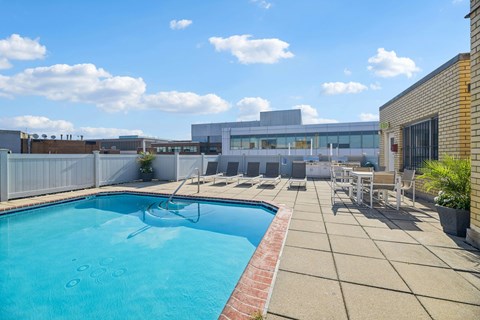 A swimming pool with a red brick border and a patio area with chairs and a table.