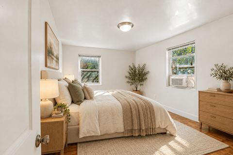 A bedroom with a bed, nightstand, and two windows.