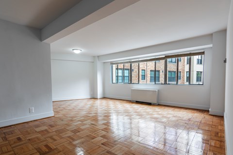 A room with wooden flooring and a window overlooking a building.
