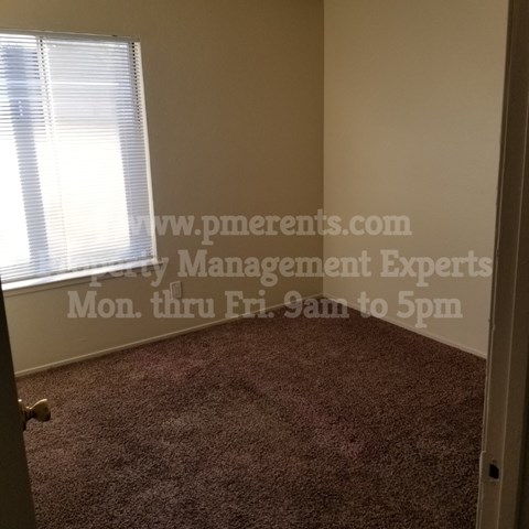 A room with a carpeted floor and a window with blinds.