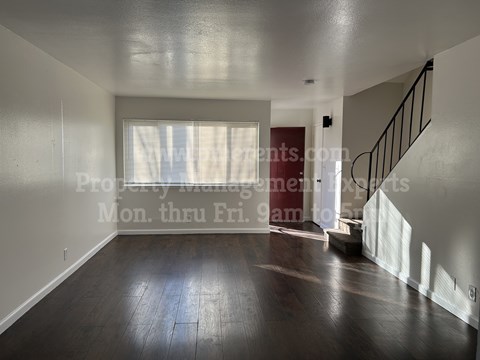 A spacious room with wooden floors and a staircase.