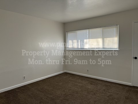 A room with a window covered by blinds and a door on the right side.