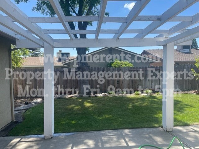 A white pergola structure is over a green lawn.