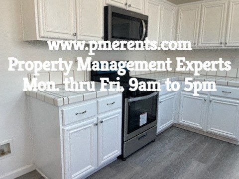 A kitchen with a microwave on top of the fridge and a website address displayed.