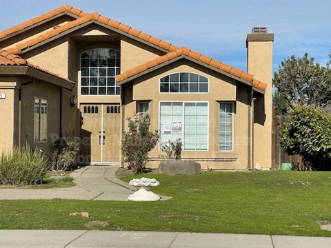 A house with a brown roof and tan walls has a white door and windows.