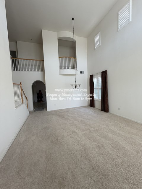A large empty room with a carpeted floor and a balcony with railings.