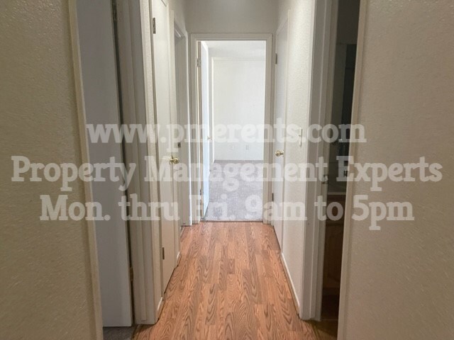 A hallway with a wooden floor and white walls leading to a door.