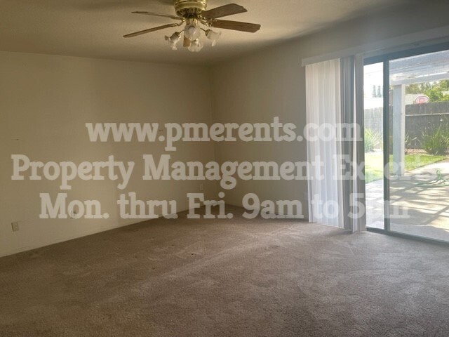 A room with a ceiling fan and a window with a view of a fence and trees.