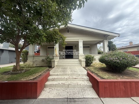 A white building with a porch and a tree in front.