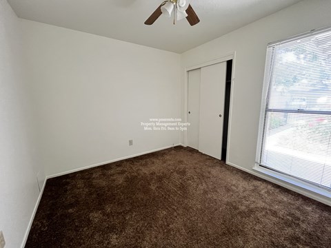 A room with a brown carpet and a ceiling fan.