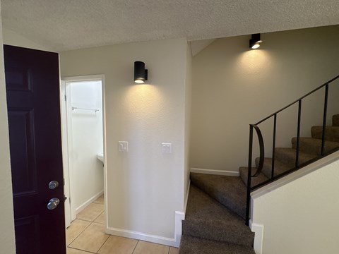 A hallway with a staircase and a black door.
