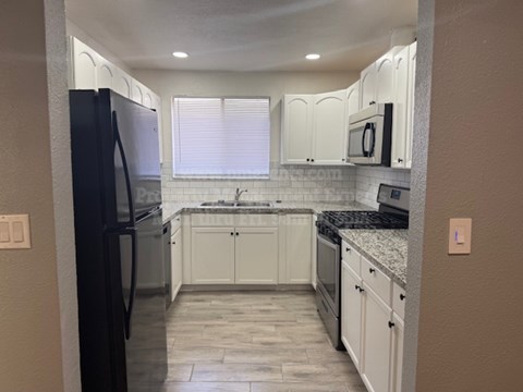 A kitchen with white cabinets and a black refrigerator.