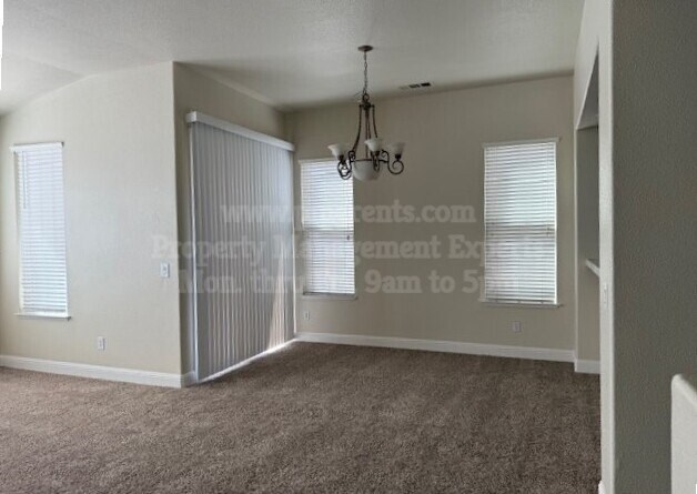 A room with a carpeted floor, a chandelier, and a window with blinds.