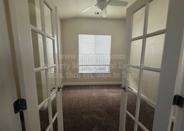 A room with a carpeted floor, a ceiling fan, and a window with blinds.