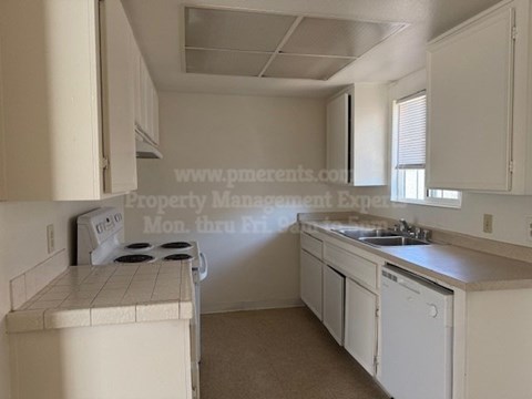 A white kitchen with a stove, sink, and cabinets.