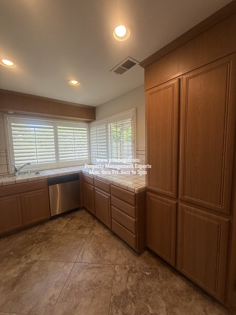A kitchen with wooden cabinets and a window with blinds.