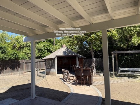 A gazebo is surrounded by a white pergola and a wooden fence.