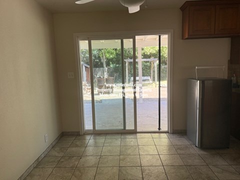A kitchen with a refrigerator and a sliding glass door leading to a backyard.