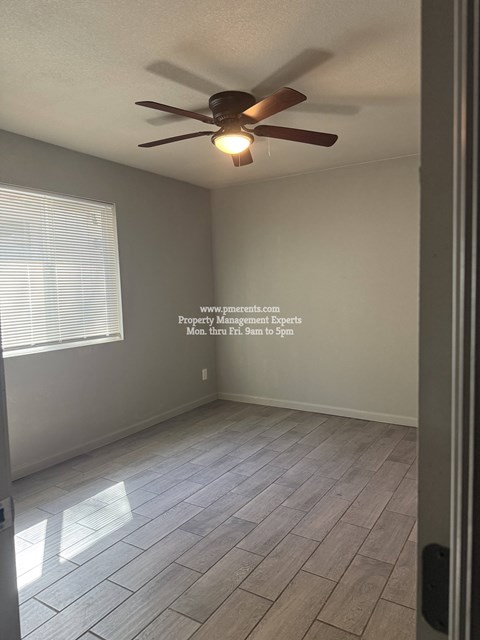 A room with a ceiling fan and light, tiled flooring, and a window with blinds.