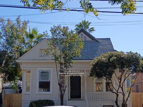 A white house with a black roof and a tree in front.