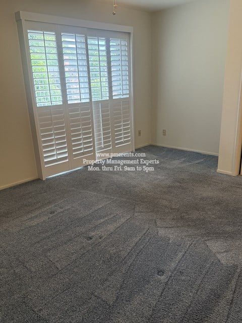 A room with a carpeted floor and a window with blinds.