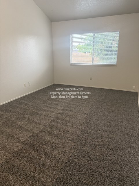 A room with a carpeted floor and a window with blinds.