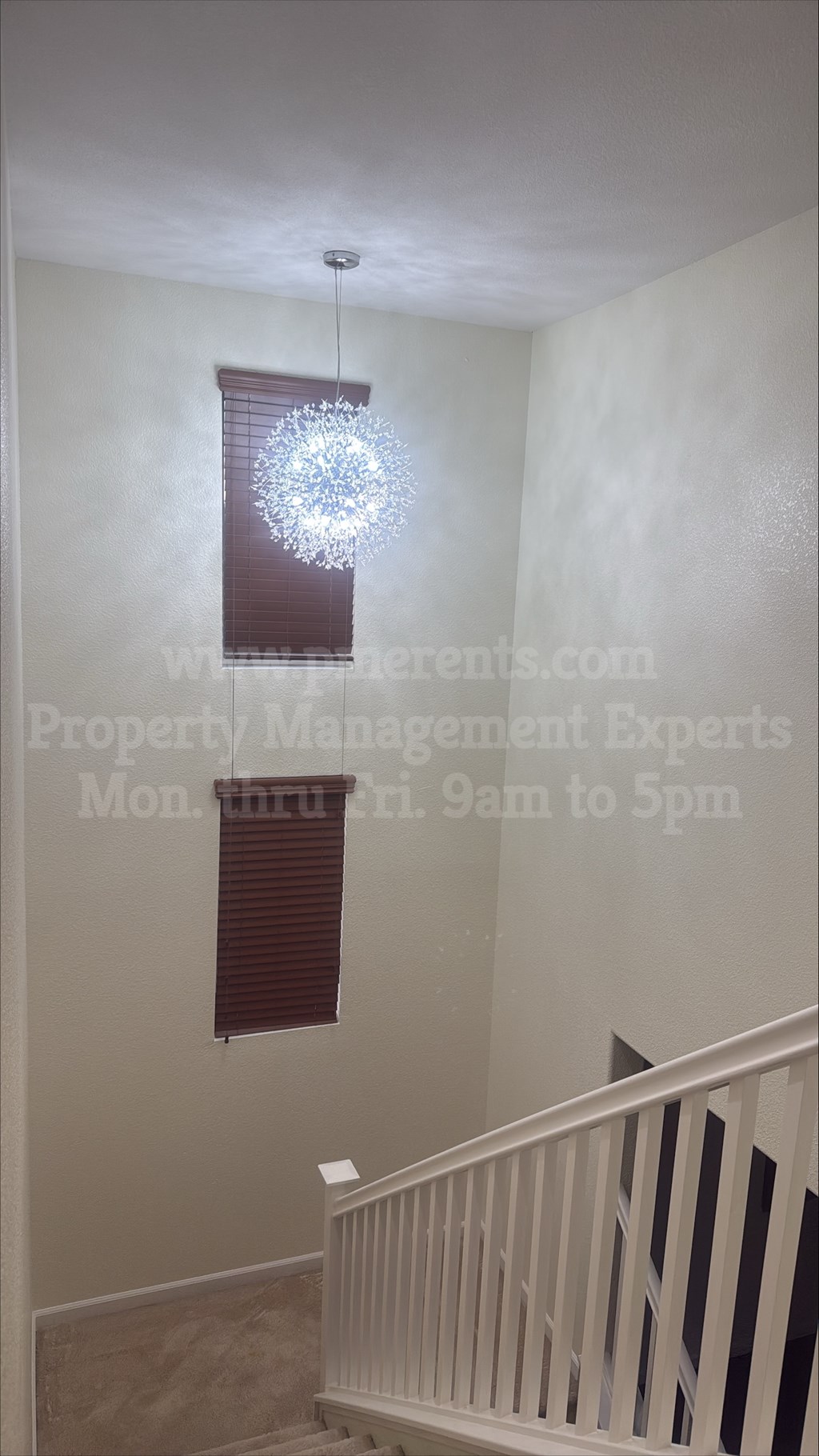 A chandelier hangs from the ceiling in a room with a staircase.
