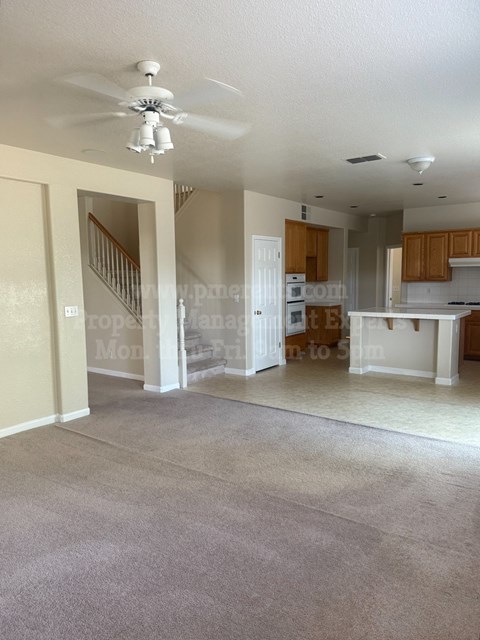 A living room with a carpet floor and a ceiling fan.