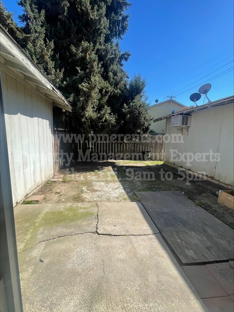 A backyard with a concrete patio and a white fence.