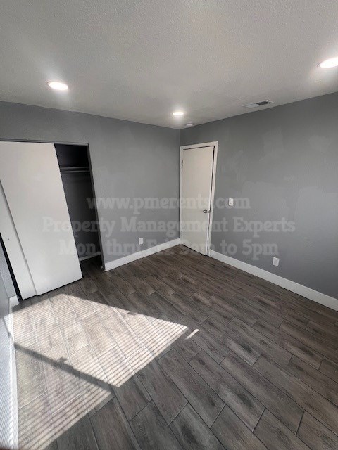A room with a grey wall and a wooden floor with a mat in front of it.