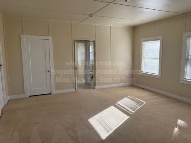 A room with a carpet, a door, a window, and a wall with a window.