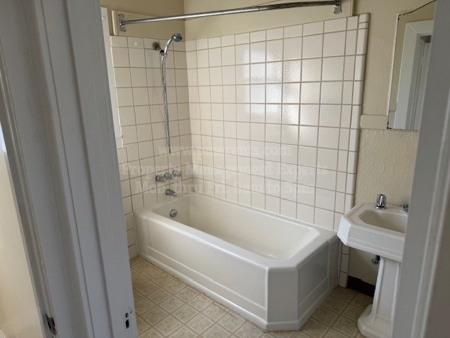 A white bathroom with a white tub, sink, and tiled walls.