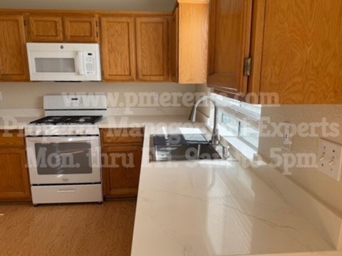A kitchen with wooden cabinets and a white microwave above the stove.