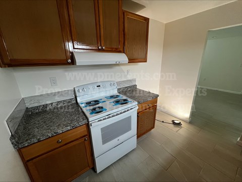 A kitchen with a white stove top oven and wooden cabinets.