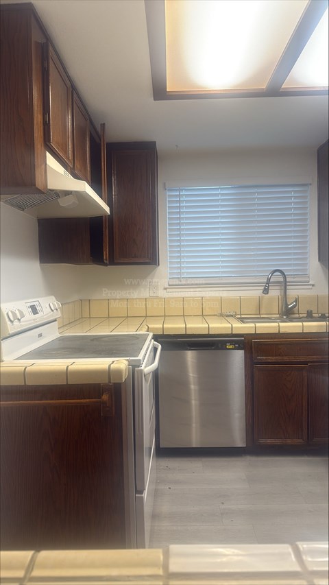 A kitchen with a stainless steel dishwasher and wooden cabinets.