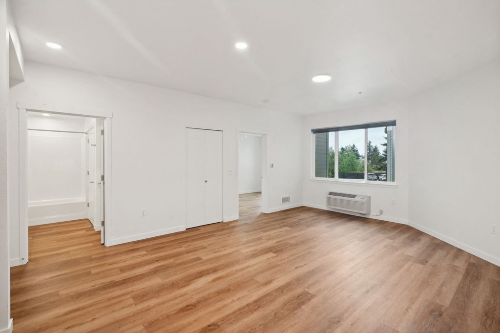 a living room with white walls and wood floors and a window