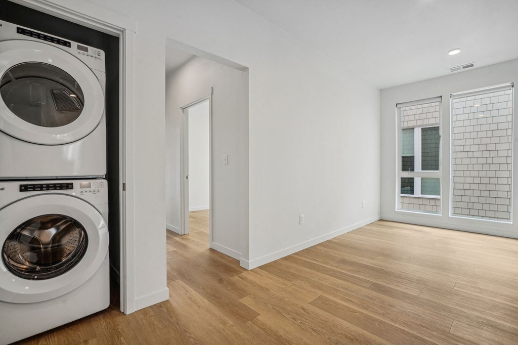 a white laundry room with a washing machine and a wood floor