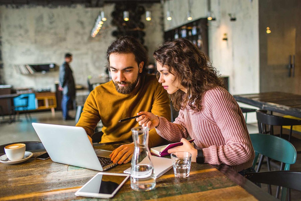 a man and woman sitting at a table looking at a laptop computer