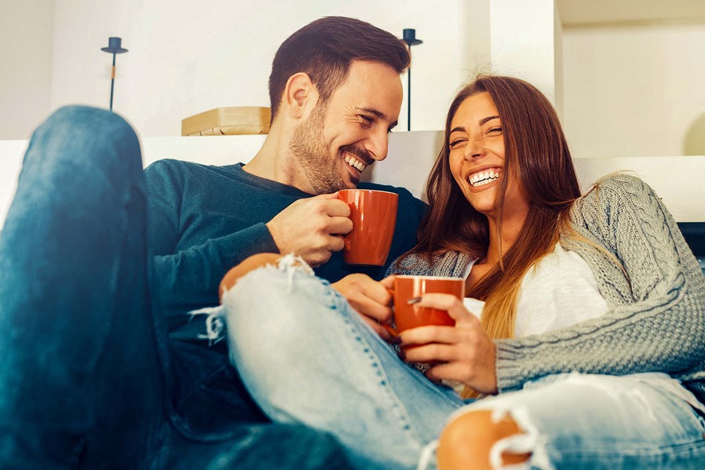 a man and woman sitting on a couch holding coffee cups