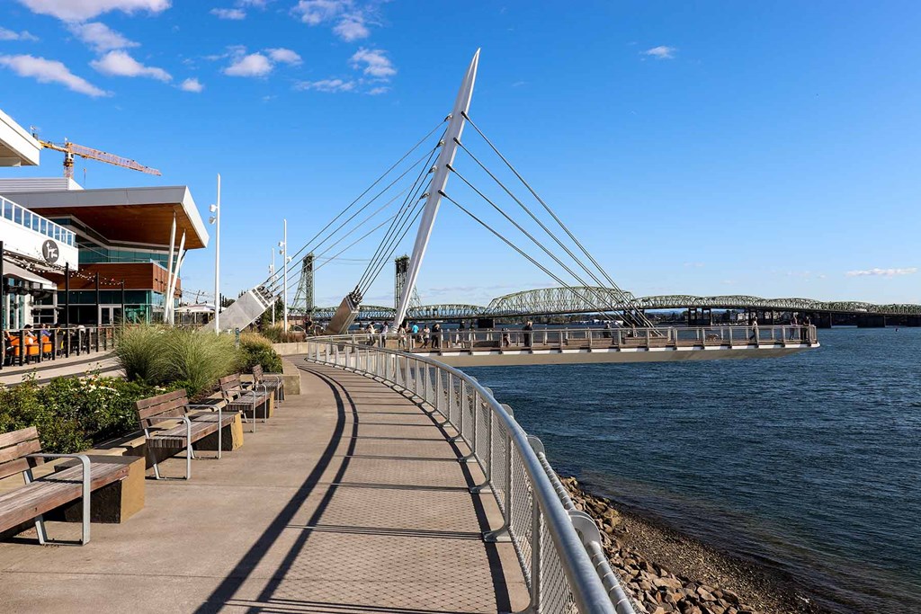 a boardwalk next to the water with benches and a bridge