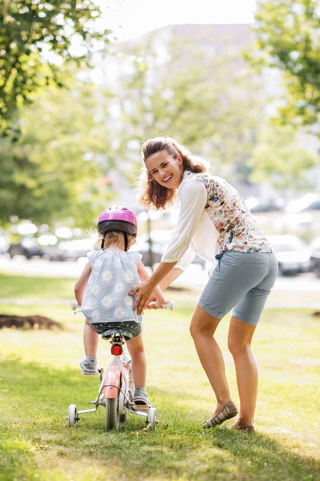Child riding bike while woman helps looking back at camera